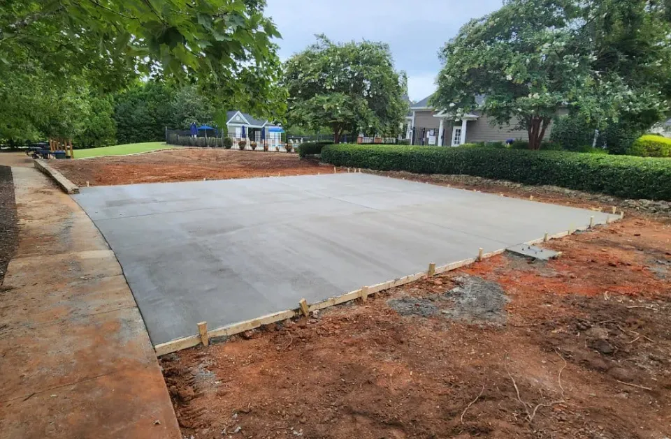 Freshly poured concrete pad surrounded by dirt, wooden forms, and greenery.