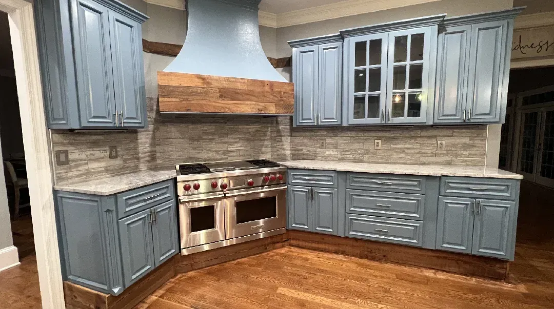 Blue kitchen cabinets with a wooden range hood over a stainless steel stove.