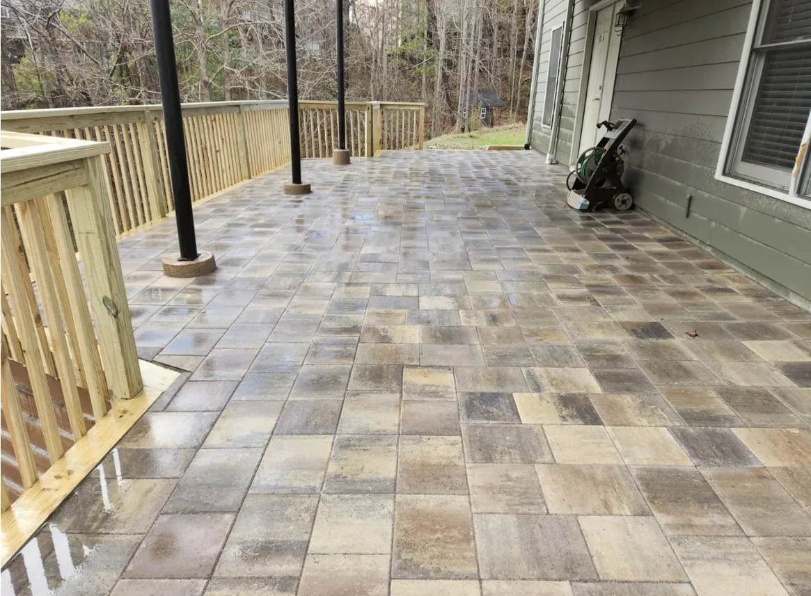 Stone-paved deck with wooden railing, extending from a house. Overcast day.