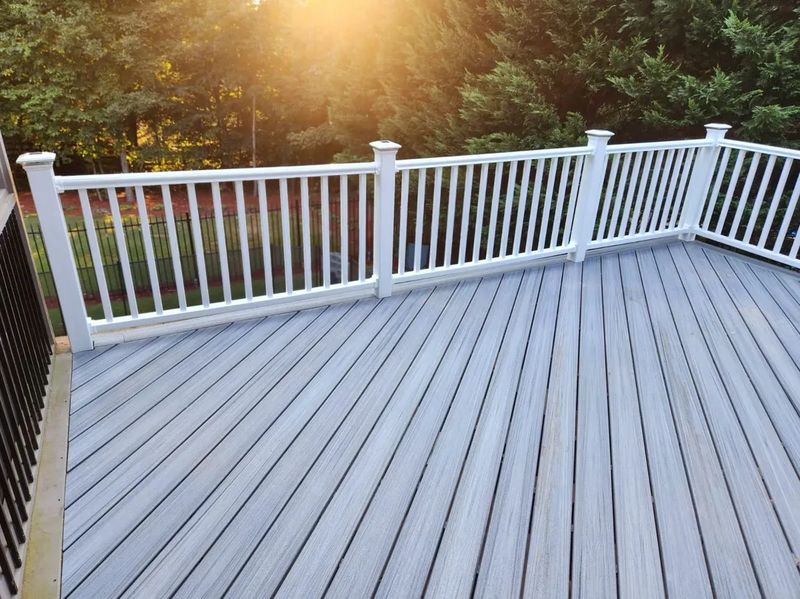 Gray deck with white railing, sunlit trees in the background.