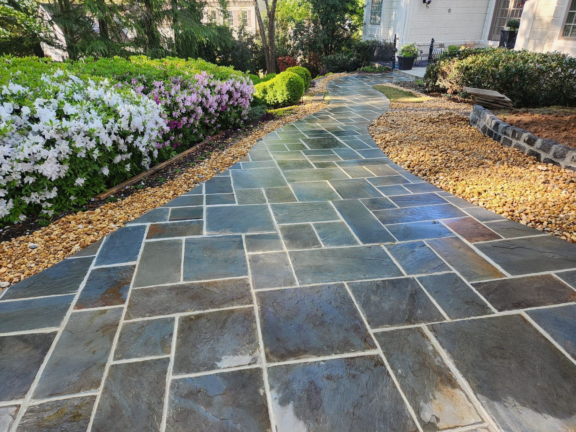 Stone walkway winding through a garden with bushes and gravel borders.
