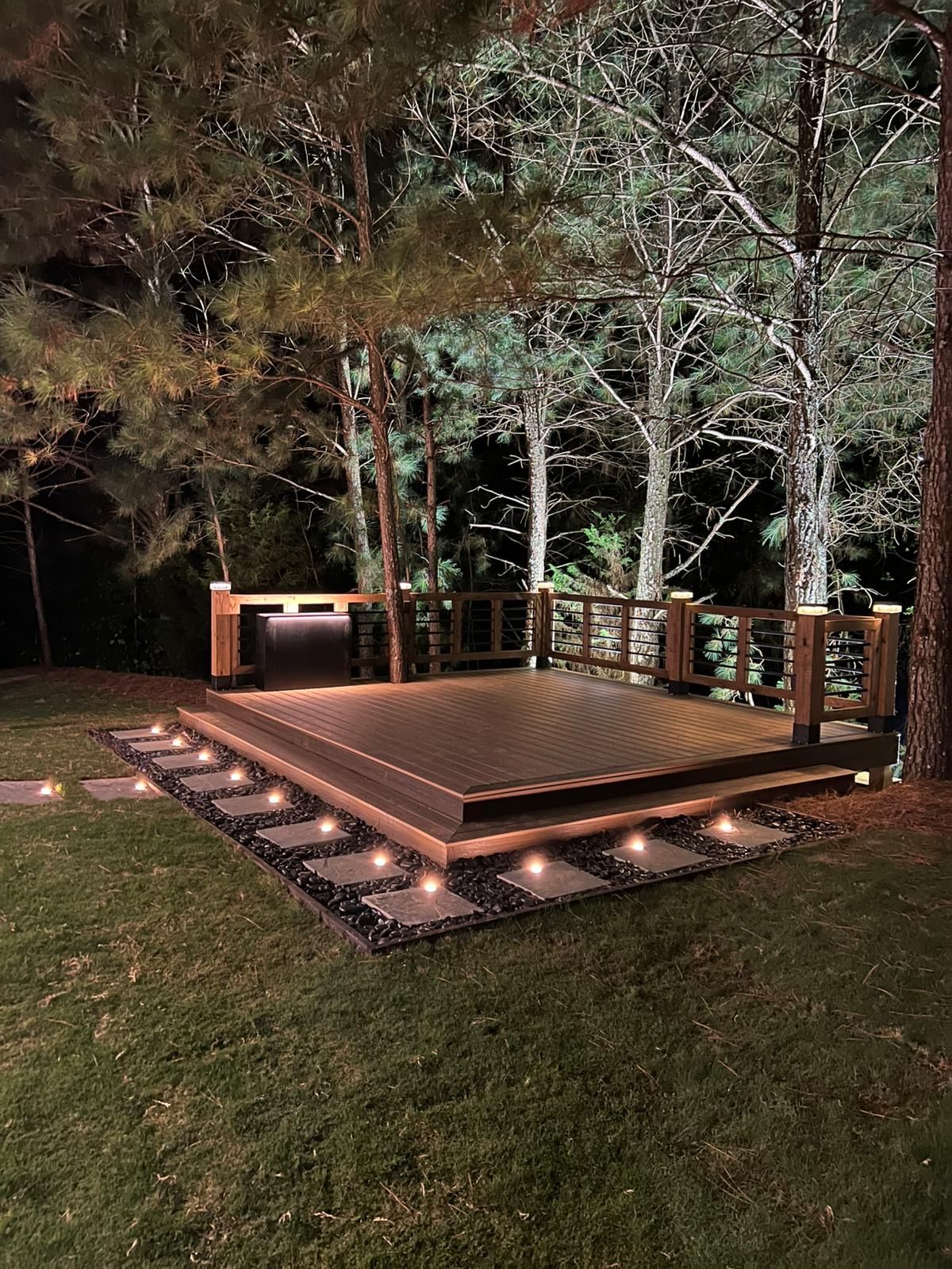 Nighttime outdoor spa deck with built-in lights, surrounded by trees and lawn.