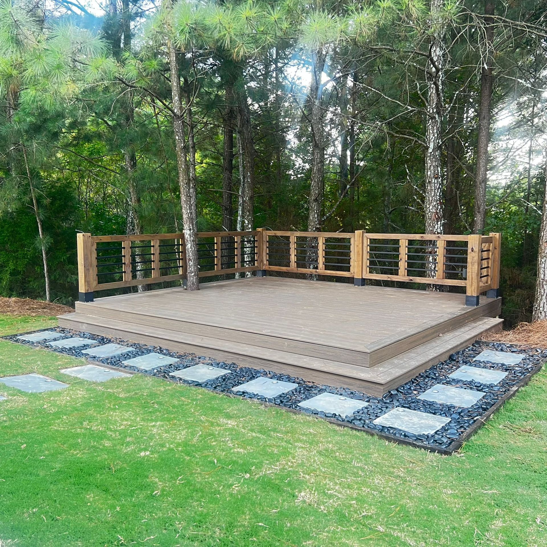 Wooden deck surrounded by trees, with stepping stones on the grass.