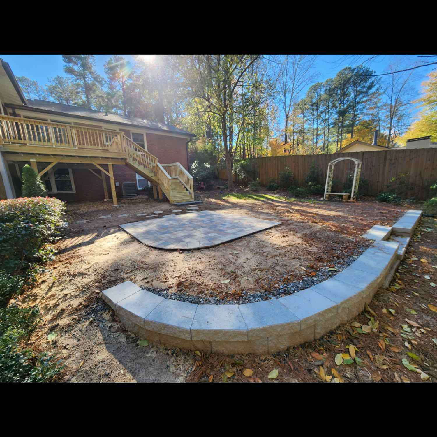 Backyard with newly built stone retaining wall and patio near a wooden deck.