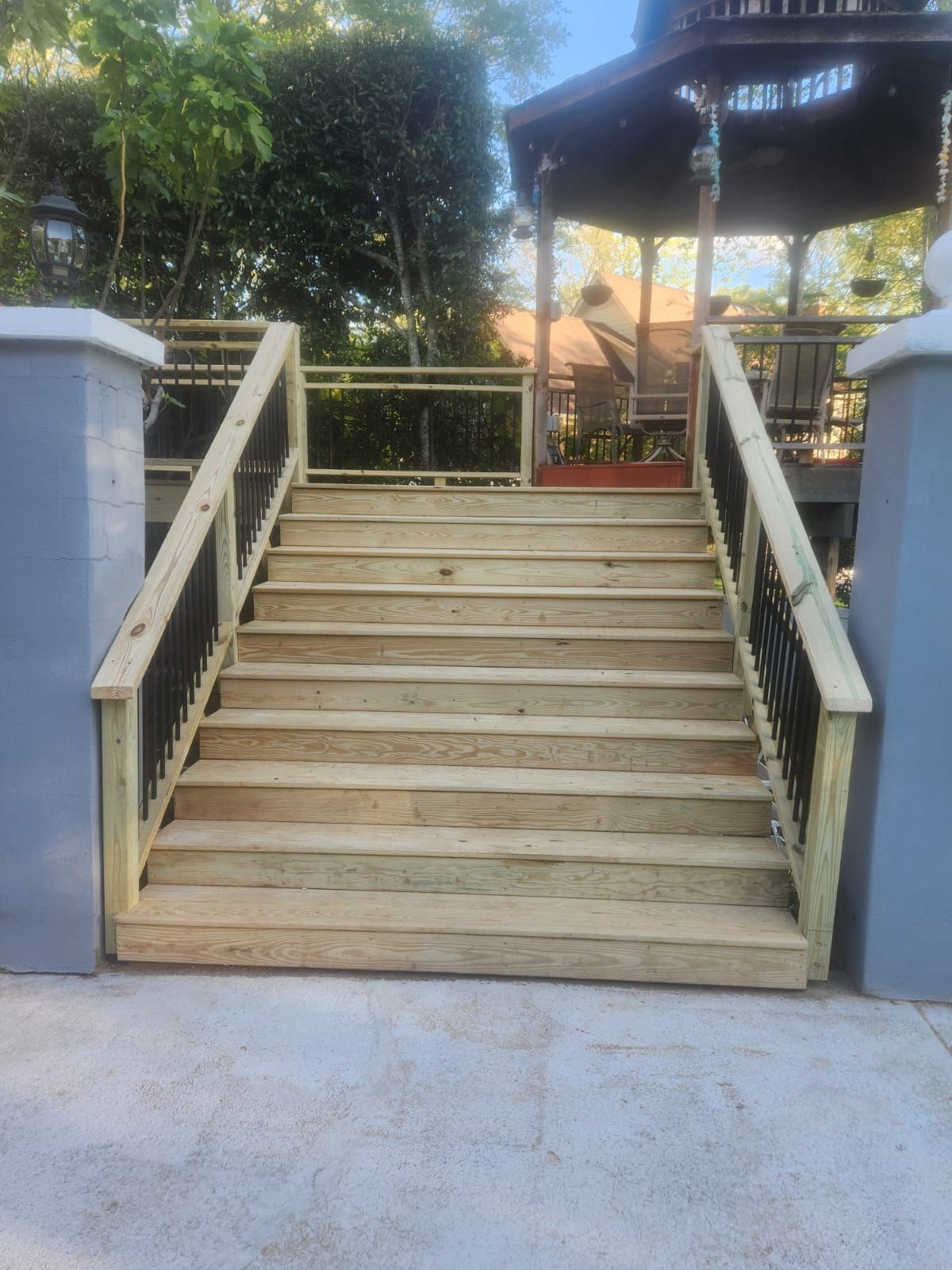 Wooden outdoor staircase leading to a gazebo. Stairs have black railings and light colored wood.