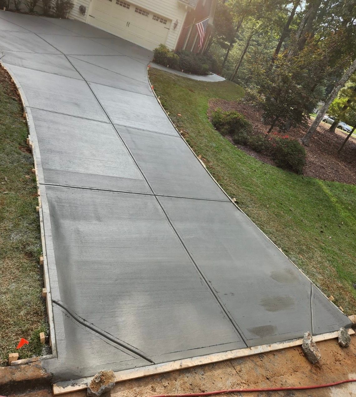 Newly poured concrete driveway, gray, curving towards a house with an American flag.