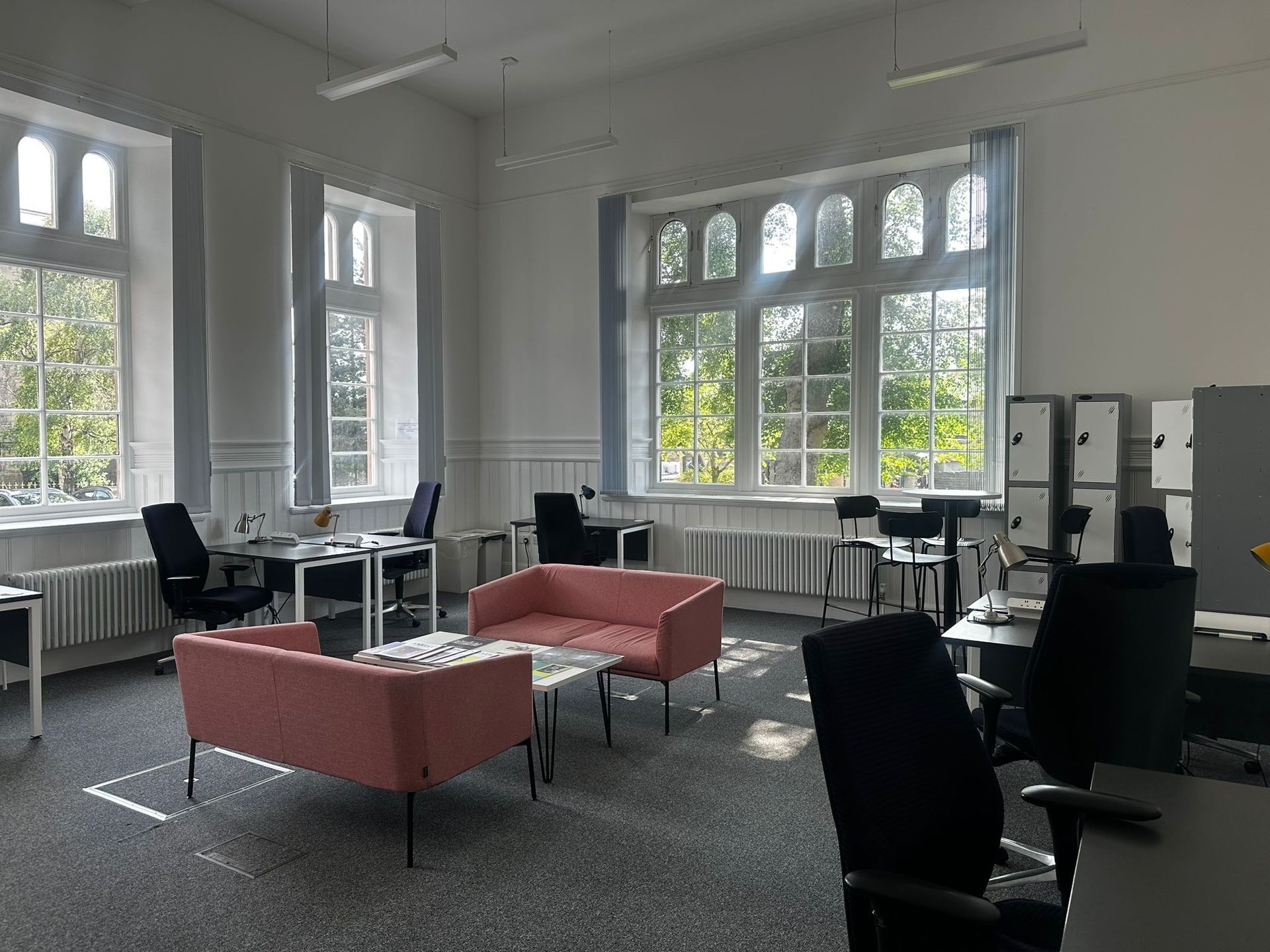 Office space with windows, desks, chairs, and pink sofa.