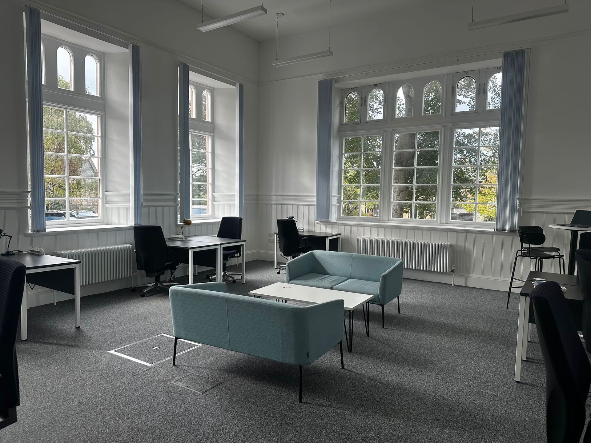 A bright, empty room with large windows, desks, and a blue sofa.