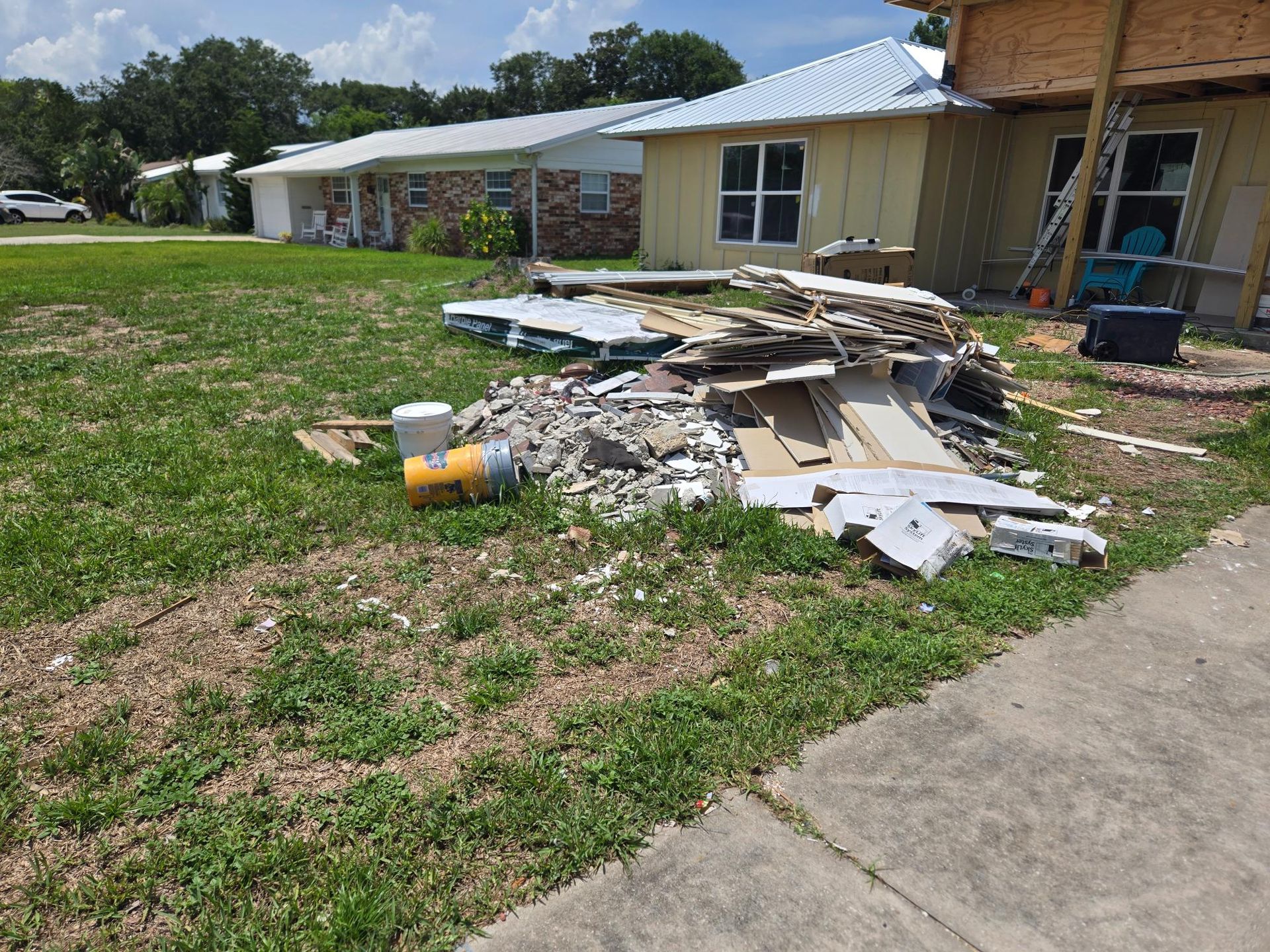 Pile of construction debris on a lawn next to a house under renovation. Yellow container visible.