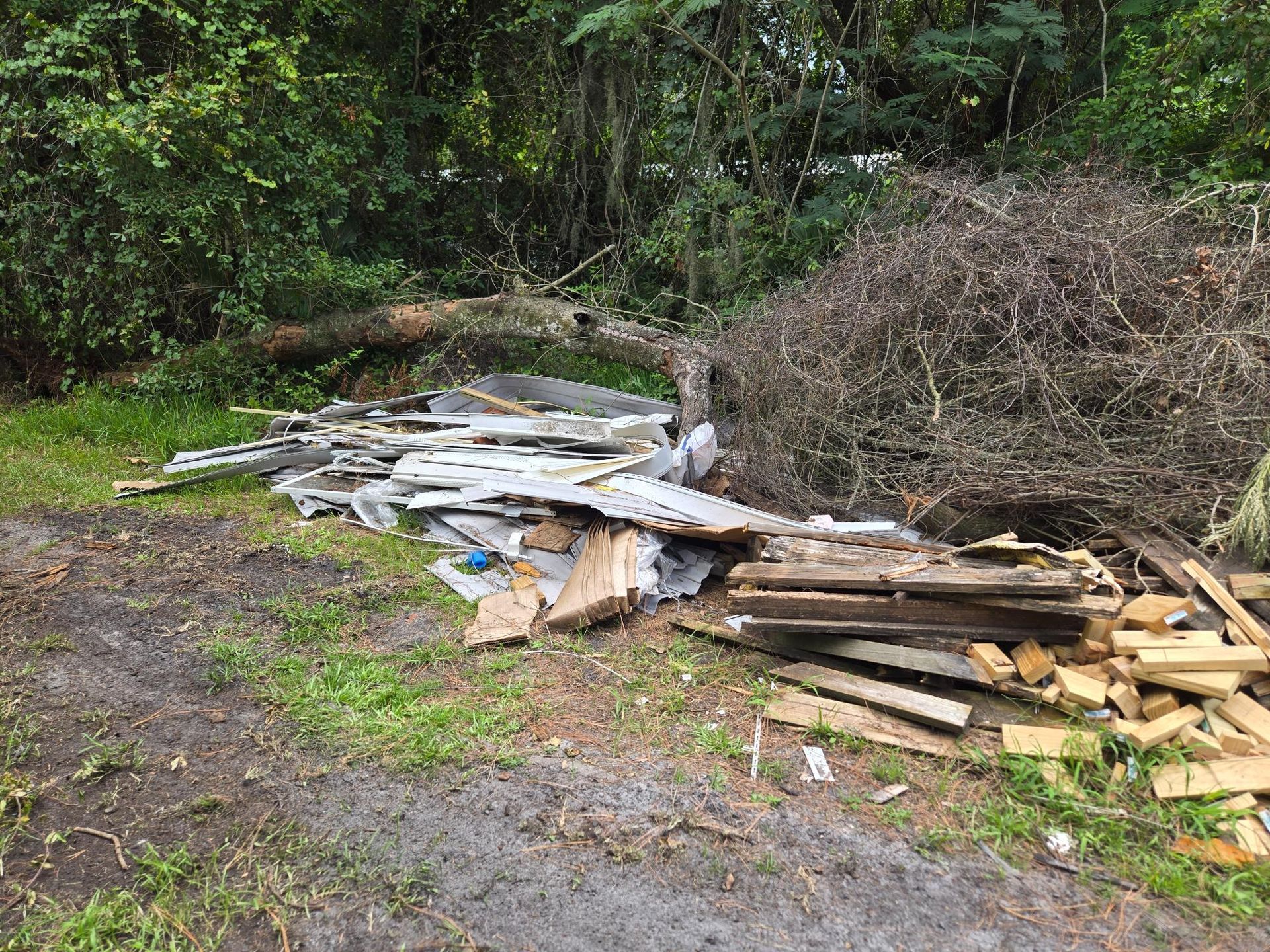 Pile of construction debris, including wood and other materials, on a grassy area with trees in the background.