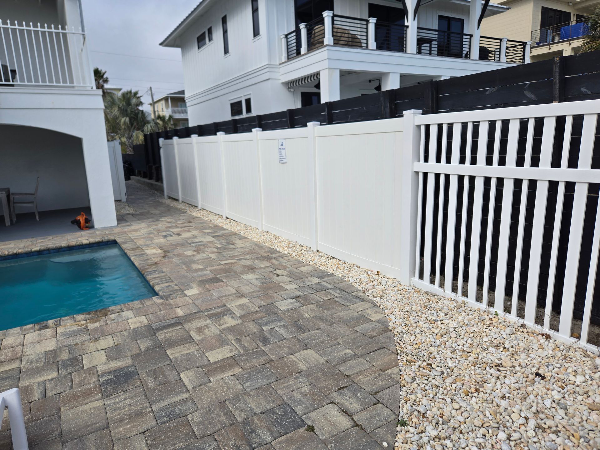 A white fence surrounds a swimming pool in front of a house.