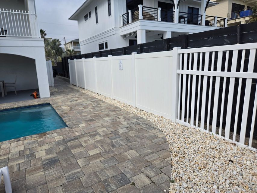 A white fence surrounds a swimming pool in front of a house.