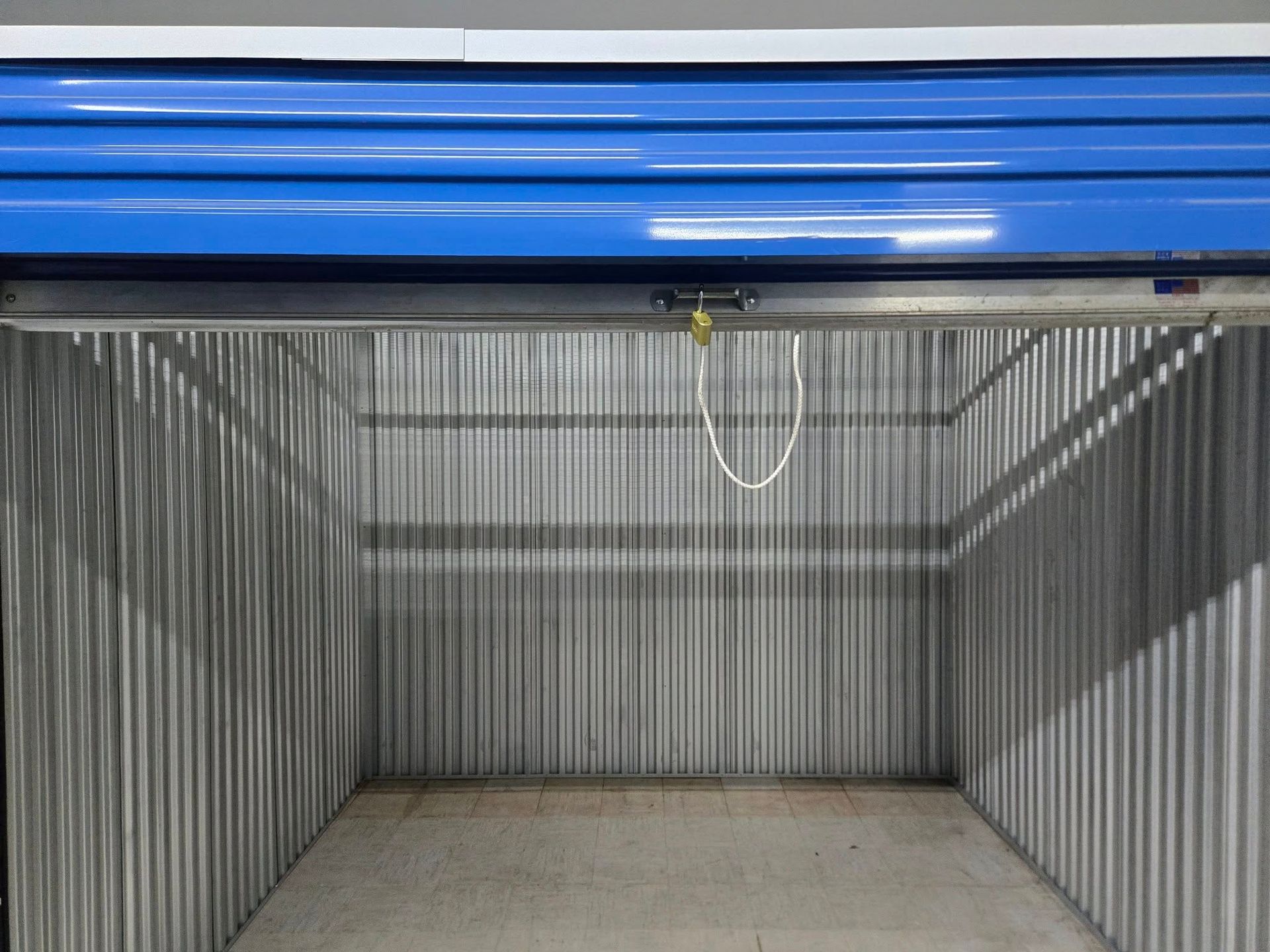 An empty storage unit with a blue door and a chain hanging from the door.