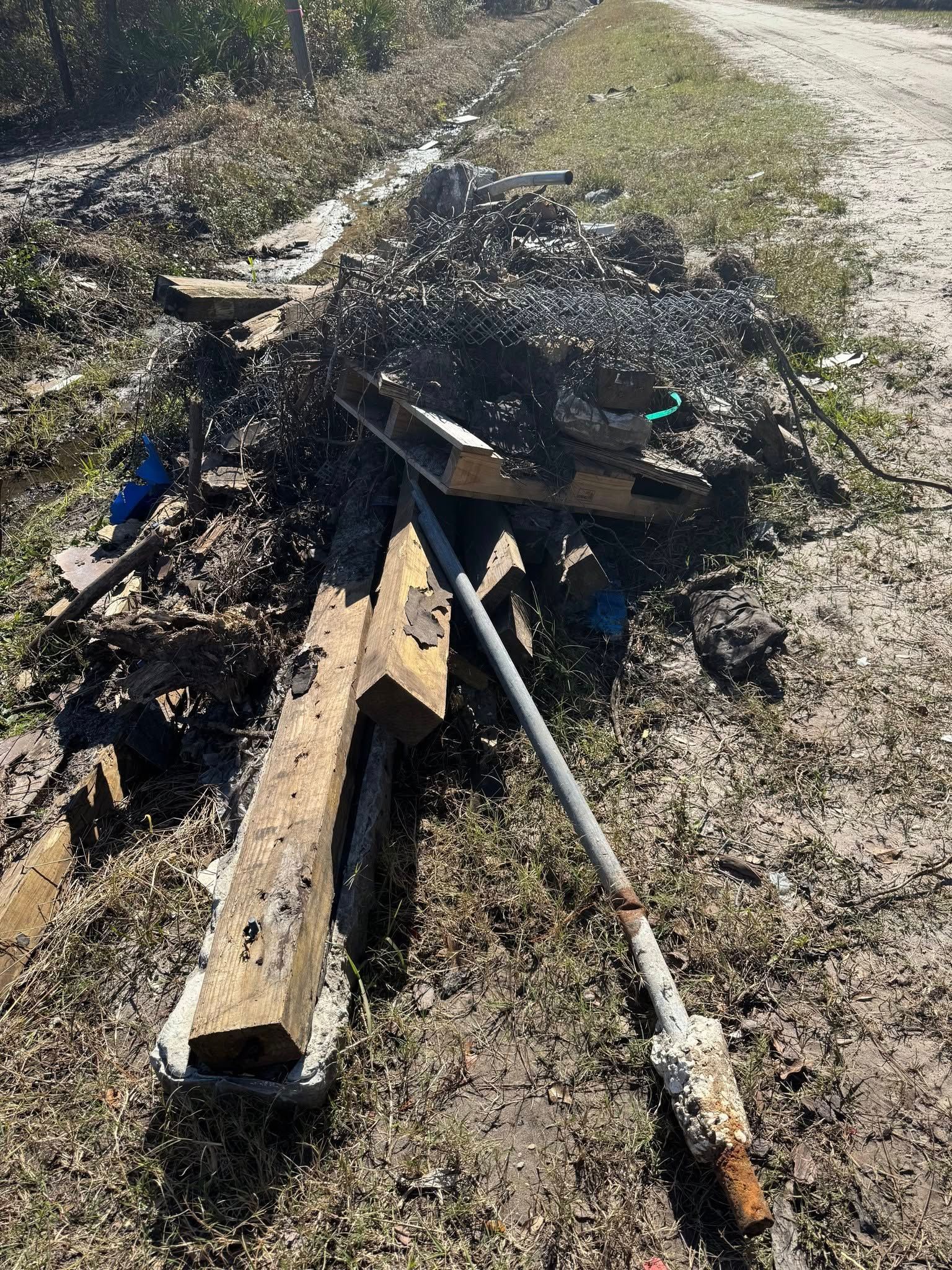 A pile of wood is sitting on the side of a dirt road.