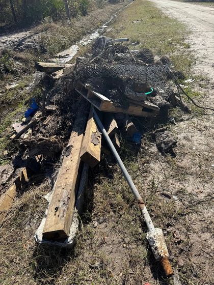 A pile of wood is sitting on the side of a dirt road.