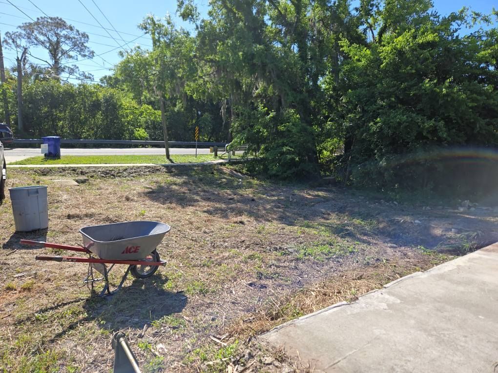 A wheelbarrow is sitting in the middle of a dirt field next to a sidewalk.