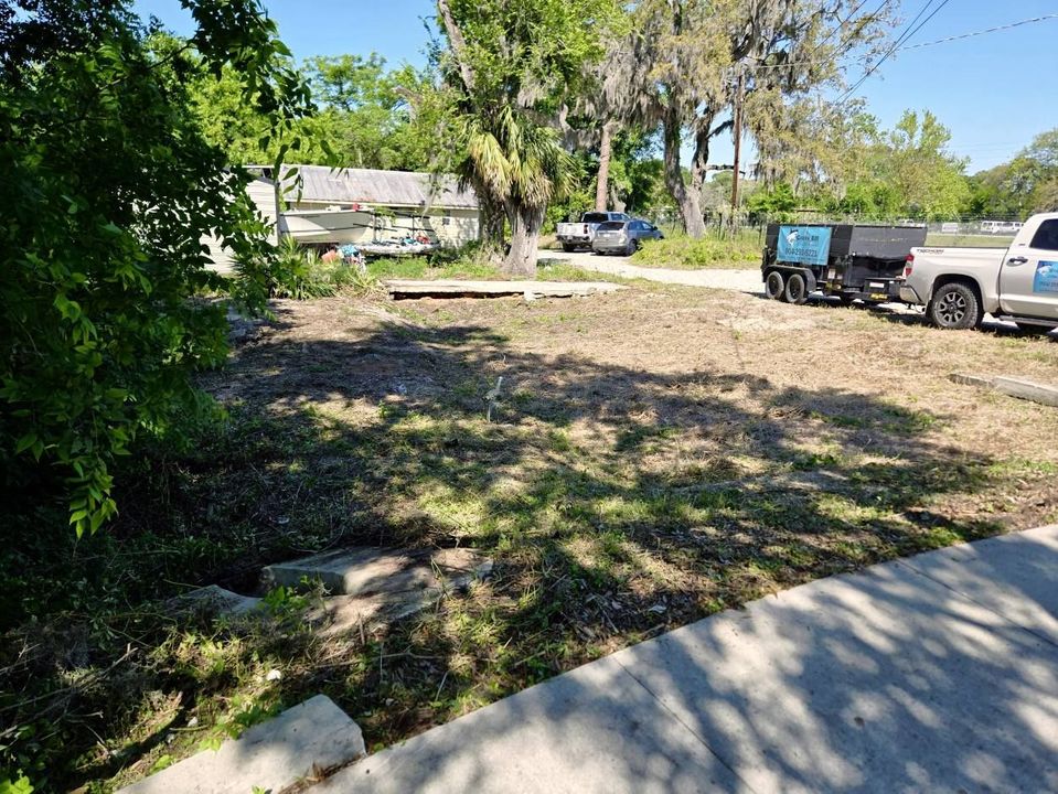A truck is parked in a dirt lot next to a sidewalk.