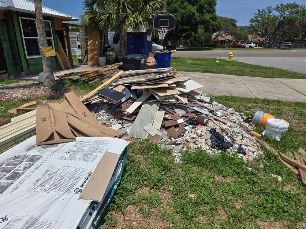 A pile of junk is sitting in the grass in front of a house under construction.