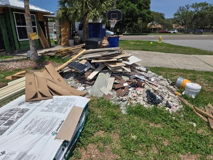 A pile of junk is sitting in the grass in front of a house under construction.