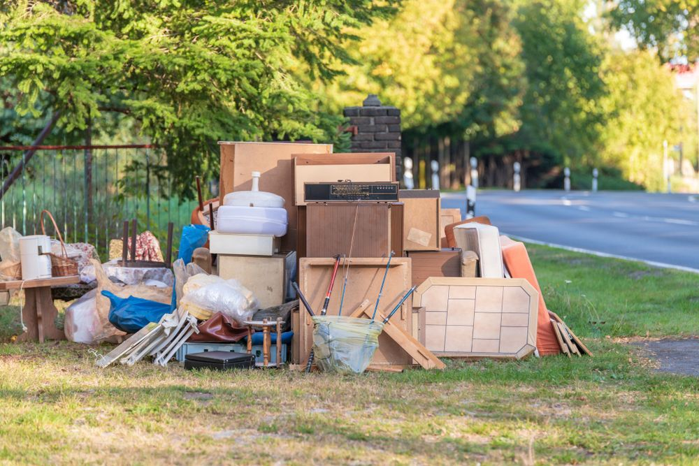 A pile of furniture is sitting on the sidewalk next to a fence.