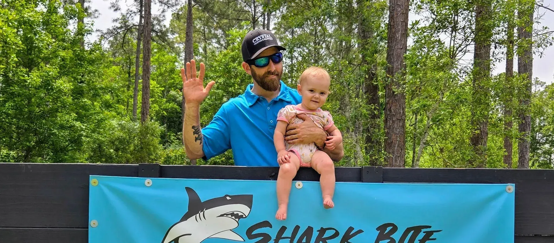 A man is holding a baby in front of a shark bite sign.