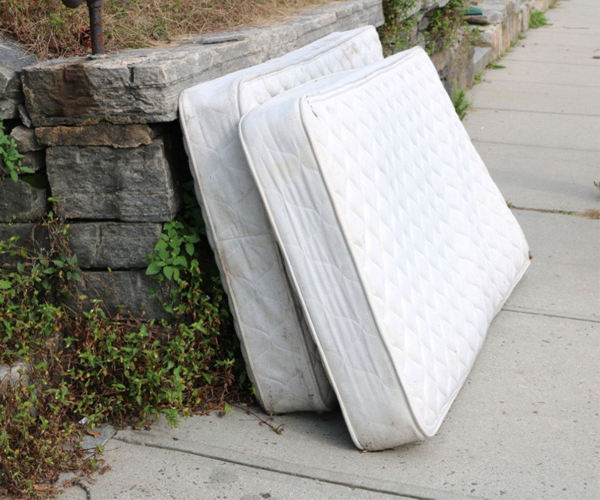 Two white mattresses are stacked on top of each other on the sidewalk
