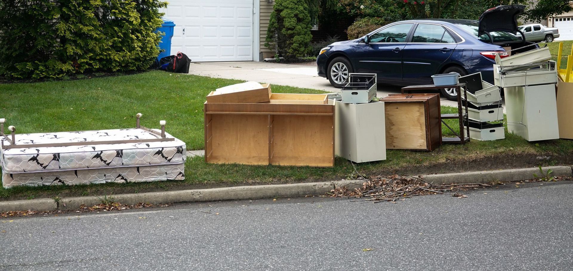 A blue car is parked on the side of the road next to a pile of junk
