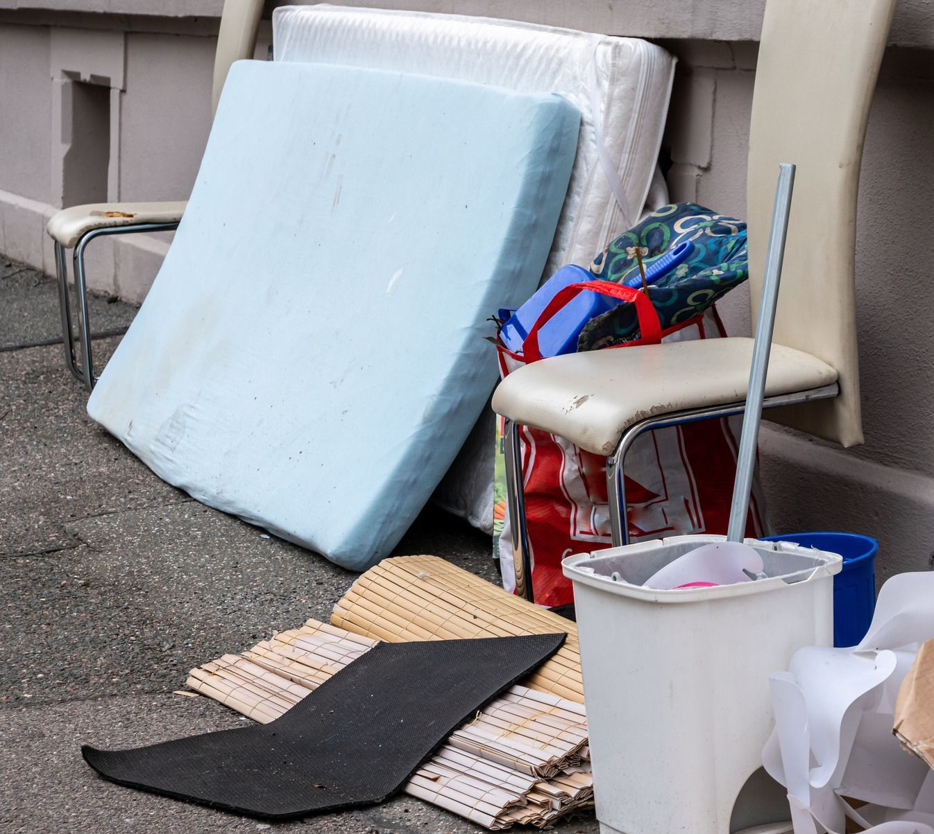 A mattress is sitting on the ground next to a chair and a trash can