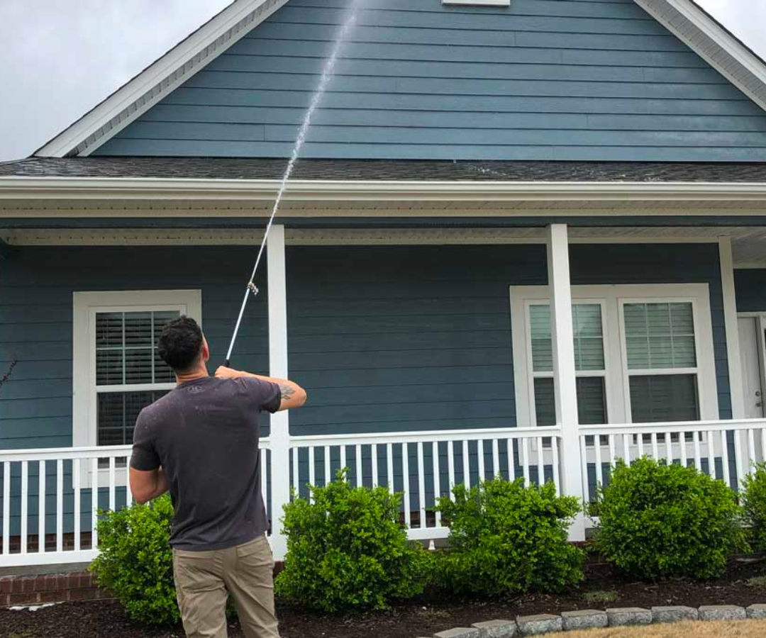A man is cleaning the side of a blue house with a pressure washer.