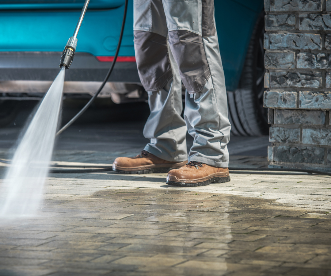 A person is using a high pressure washer to clean a driveway.