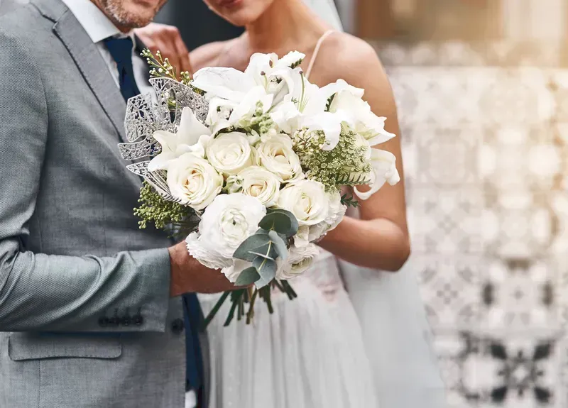 A bride and groom are standing next to each other holding a bouquet of white flowers.