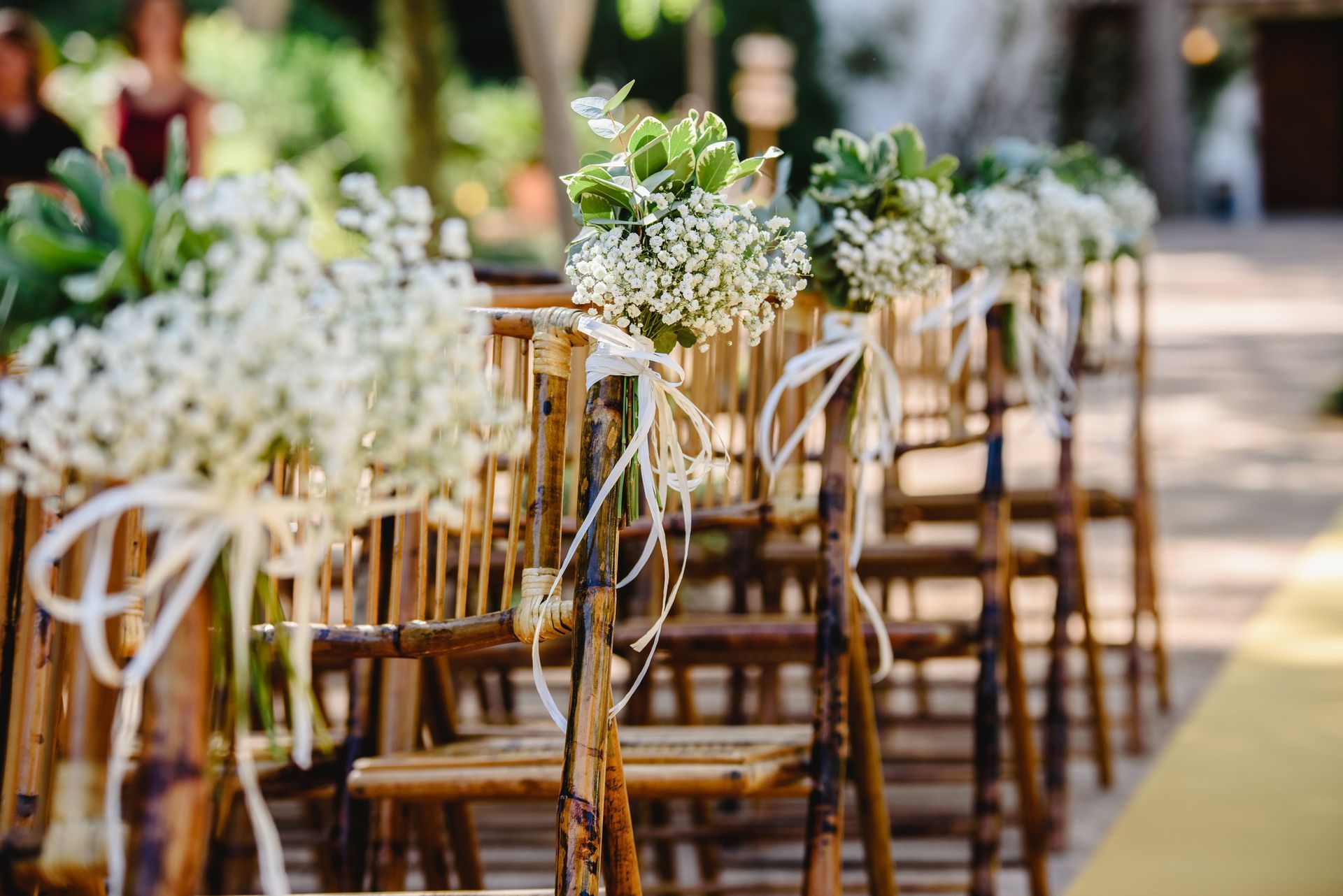 A row of wooden chairs decorated with baby 's breath and flowers for a wedding ceremony.