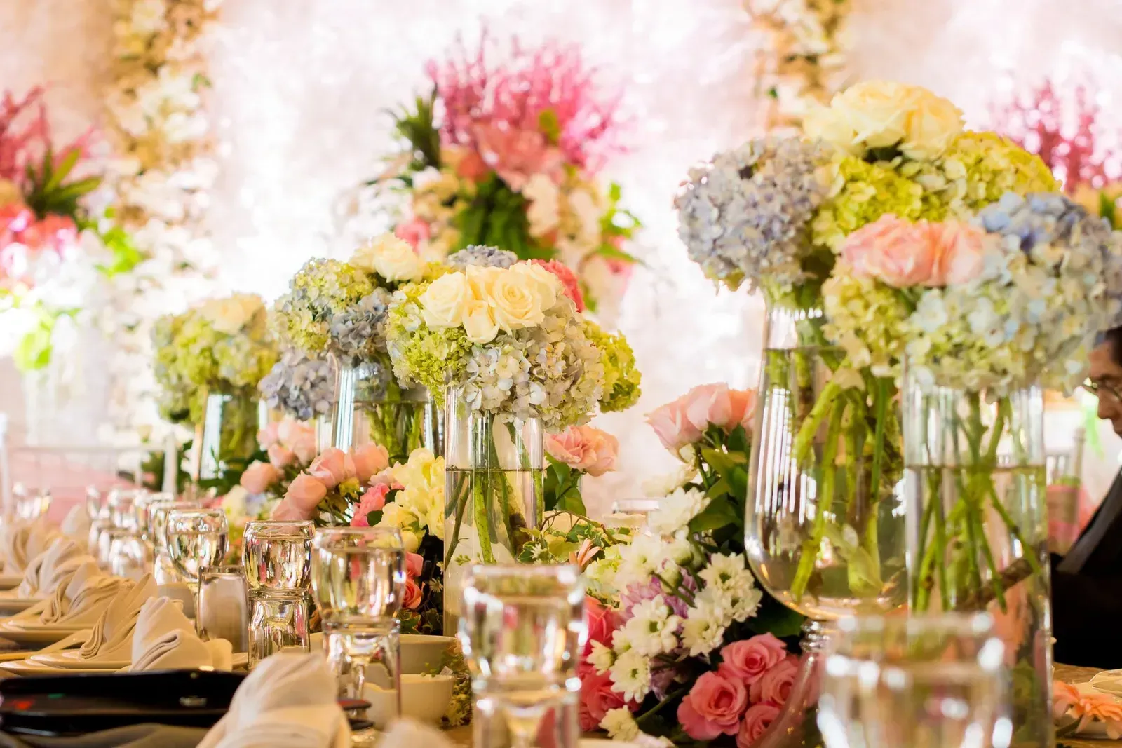 A long table decorated with vases of flowers and wine glasses.