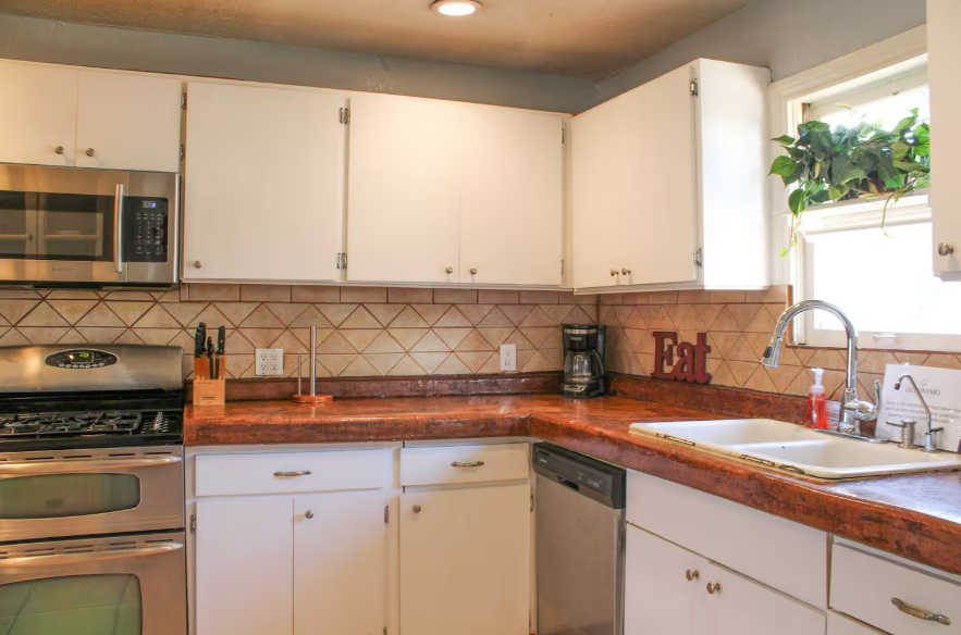 A kitchen with white cabinets , stainless steel appliances , a sink , and a window.