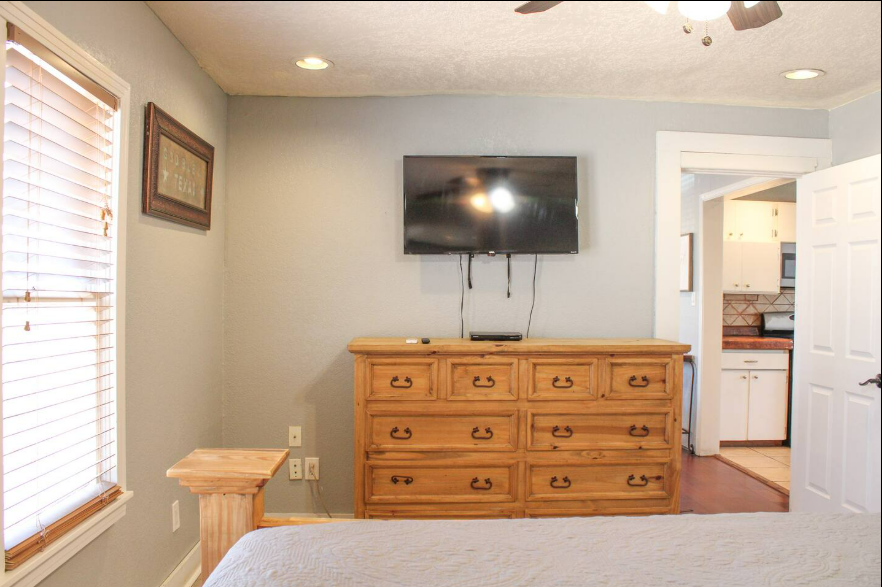 A bedroom with a dresser and a flat screen tv on the wall.