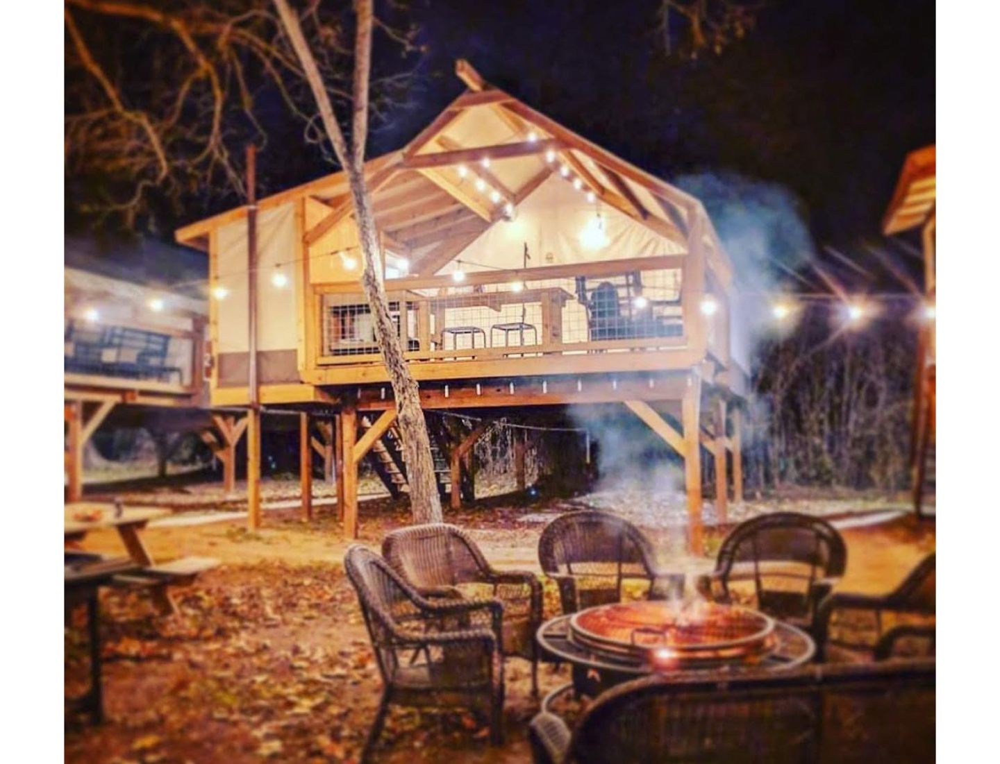 A tree house with a fire pit in front of it at night.