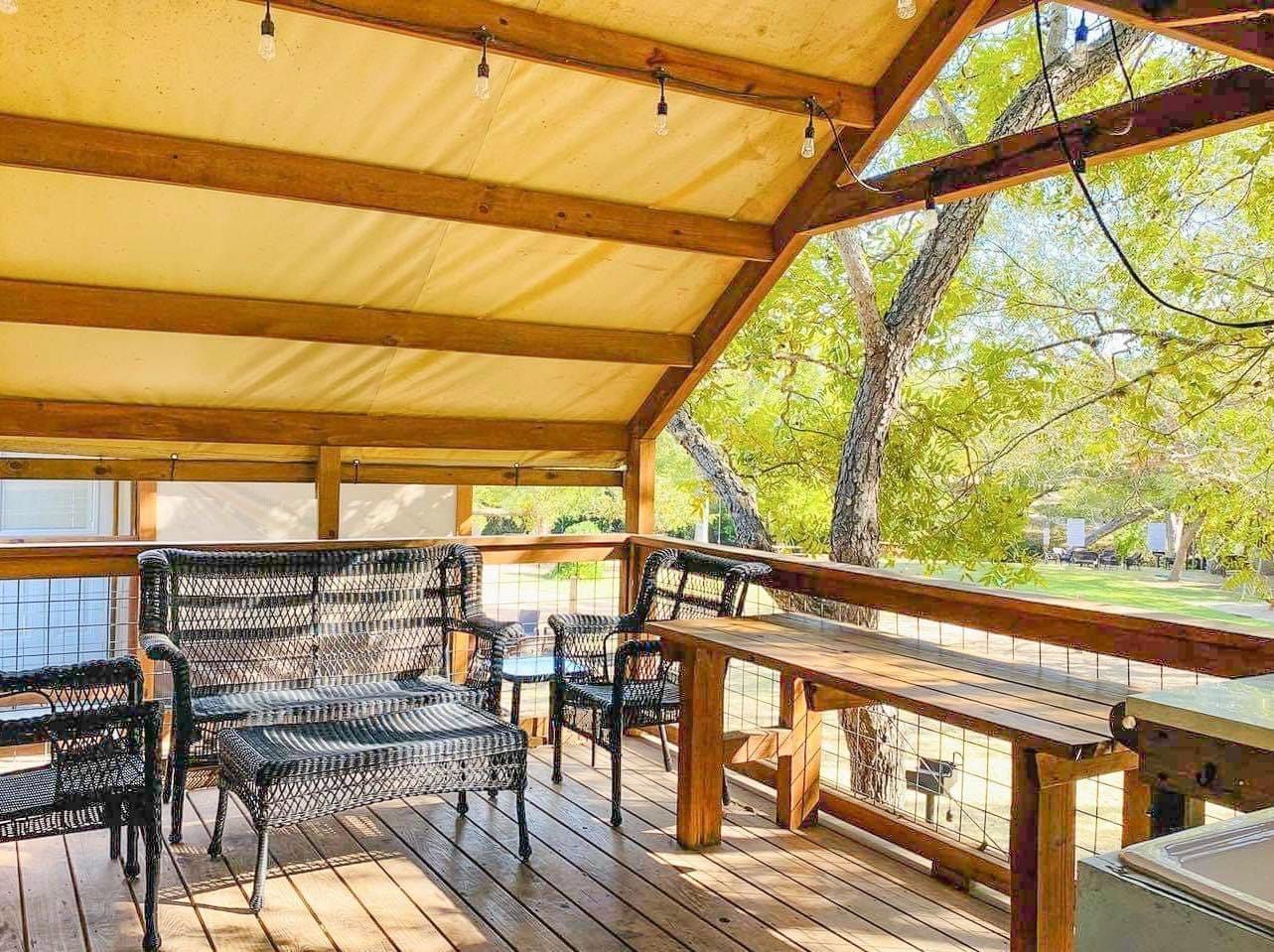 A wooden deck with a couch , chairs , and tables under a canopy.