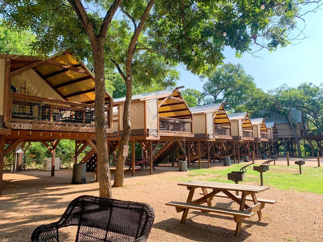 A row of tents on stilts with a picnic table in front of them.