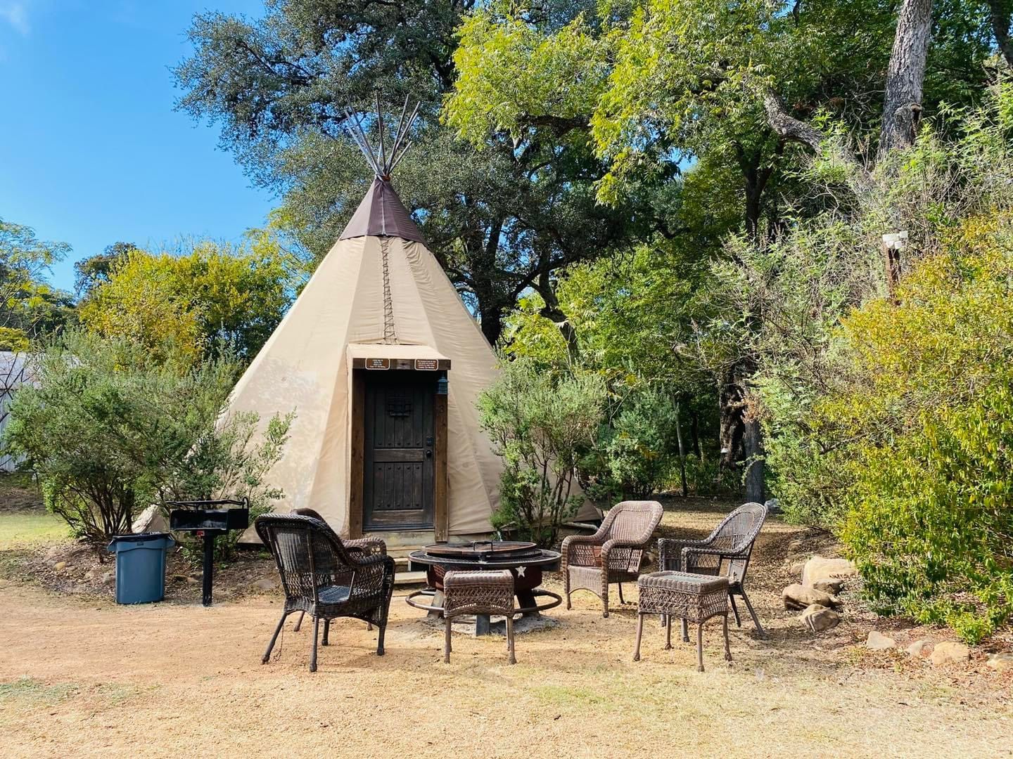 A teepee with a fire pit and chairs in front of it.