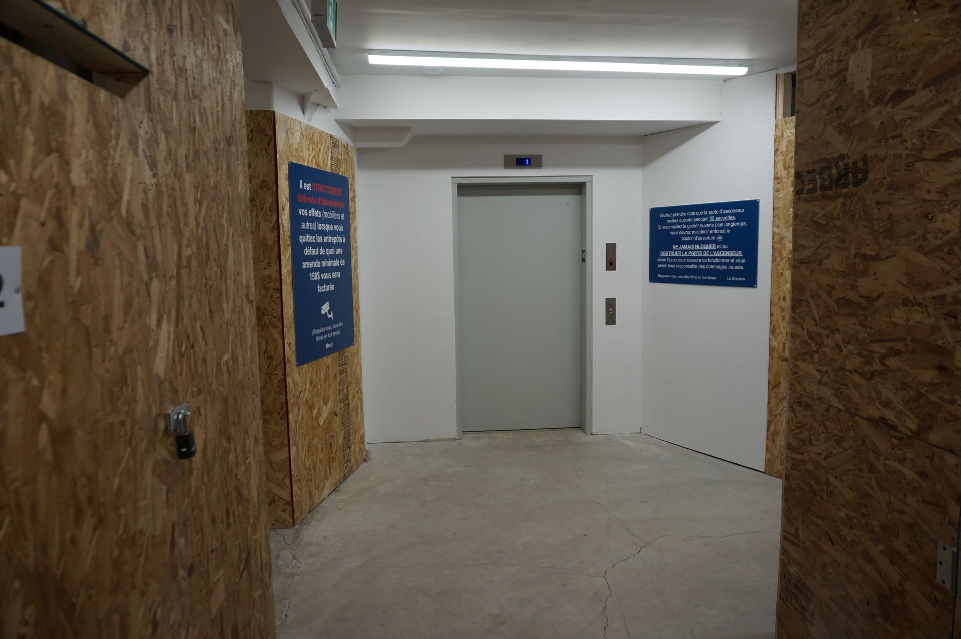 Ascenseur dans un couloir avec murs lambrissés et panneaux d'information.