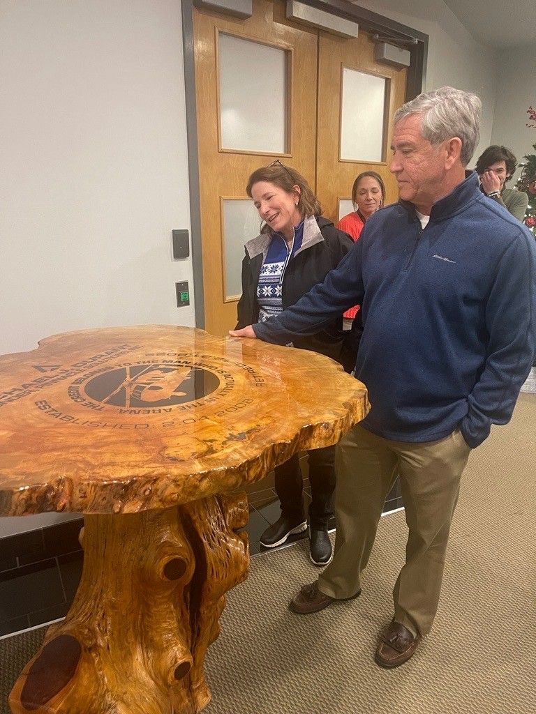 A man and a woman are standing next to a wooden table.