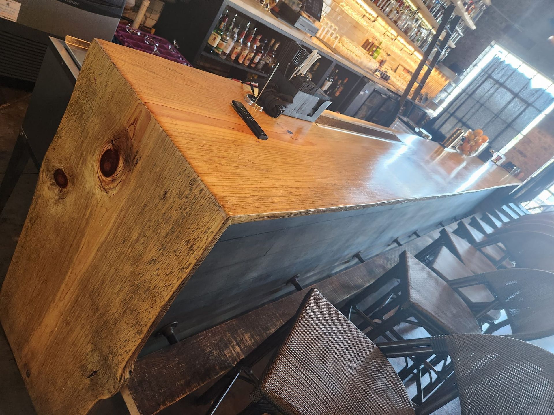 A bar with a wooden counter top and wicker chairs in a restaurant.