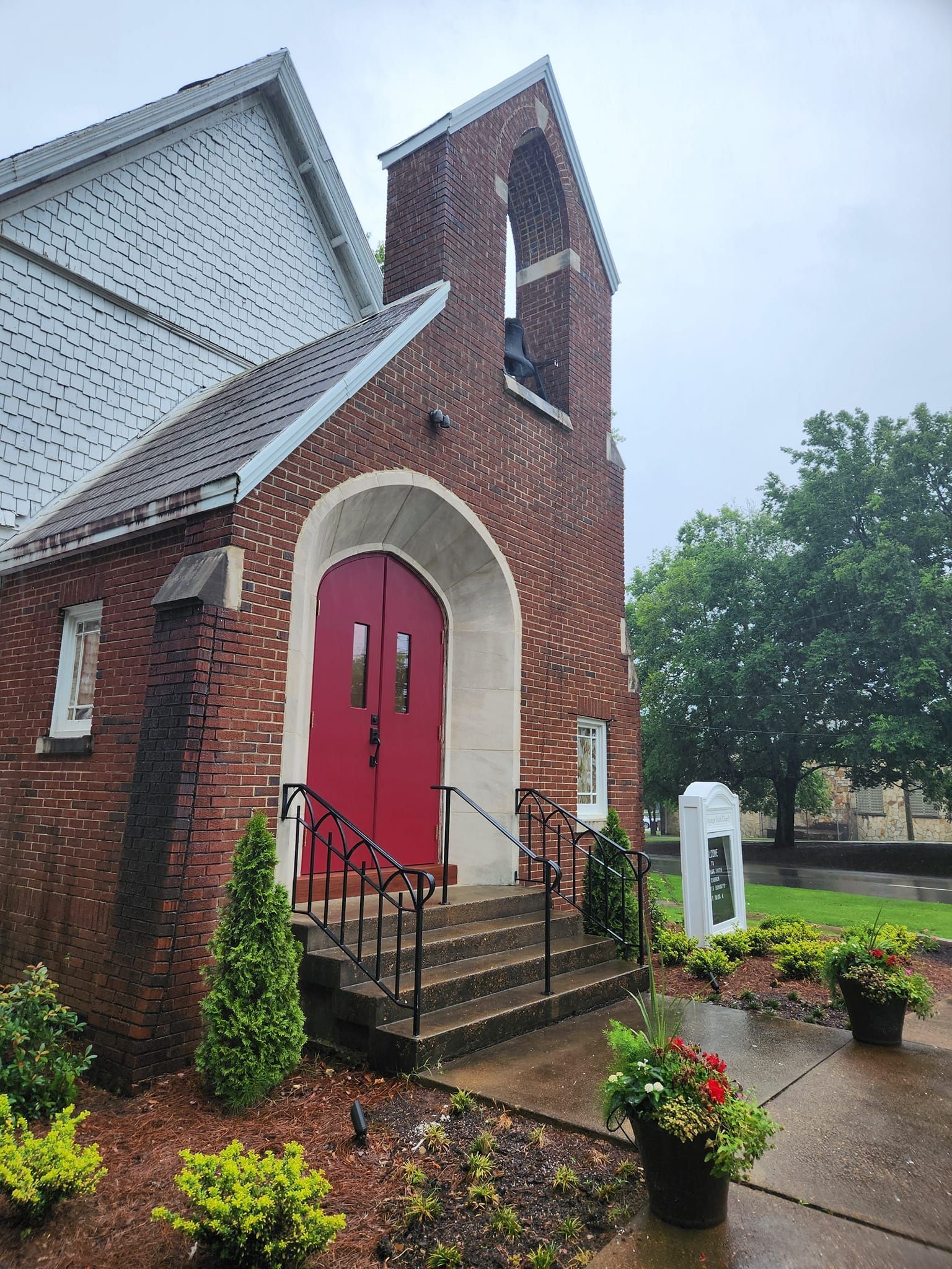 A brick church with a red door and stairs on a rainy day.