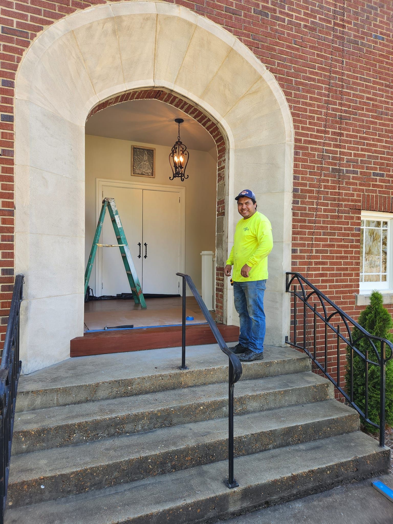 A man in a yellow shirt is standing in front of a brick building.