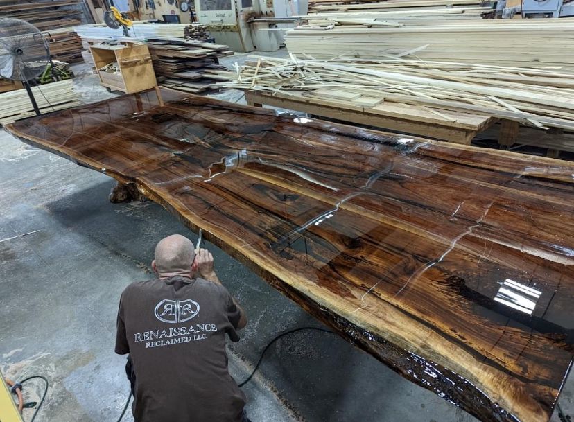 A man is working on a large piece of wood in a workshop.