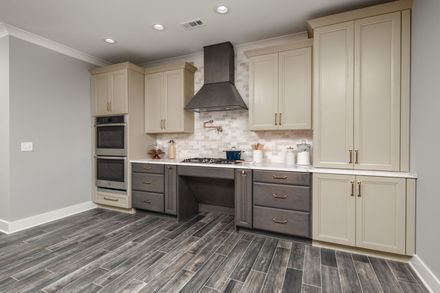 A kitchen with a stove , sink , cabinets and a wooden floor.