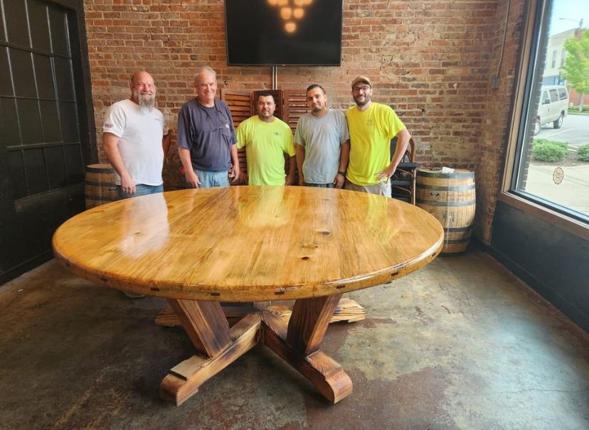 A group of men are standing around a wooden table in a room.