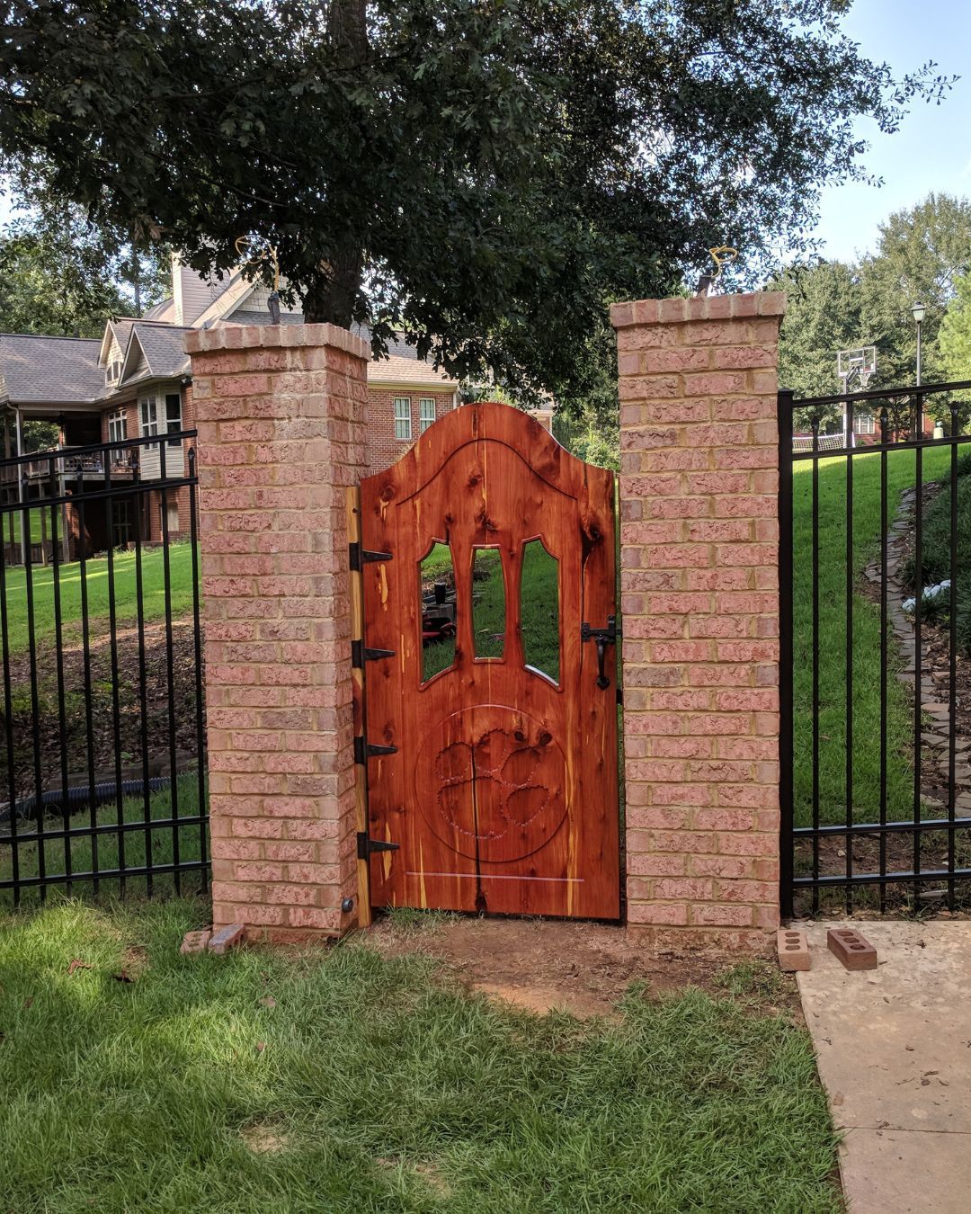 A wooden gate is surrounded by brick pillars and a metal fence.