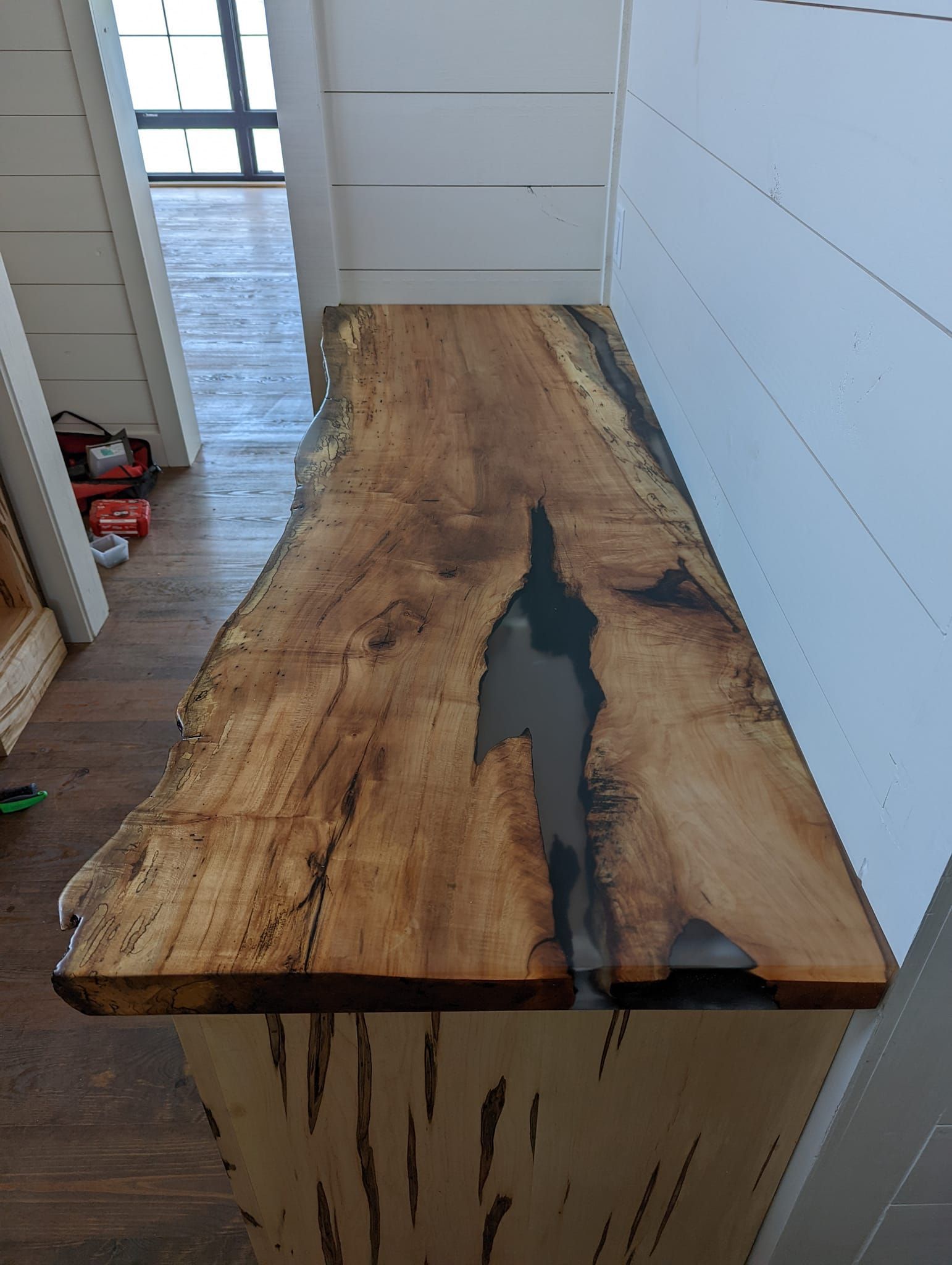 A wooden table with a gray resin in it is sitting on a wooden floor in a room.