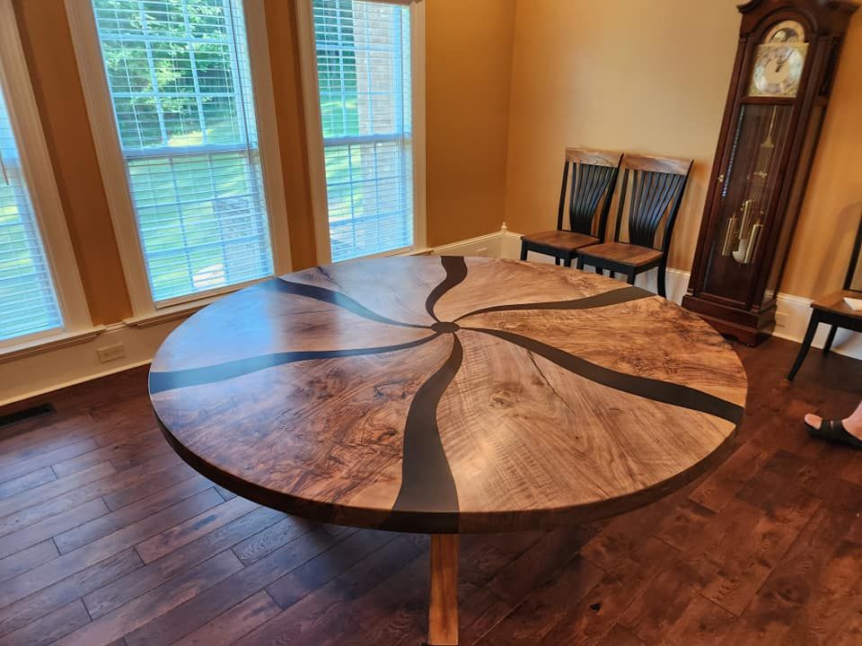 A round wooden table is sitting in a dining room next to a clock.